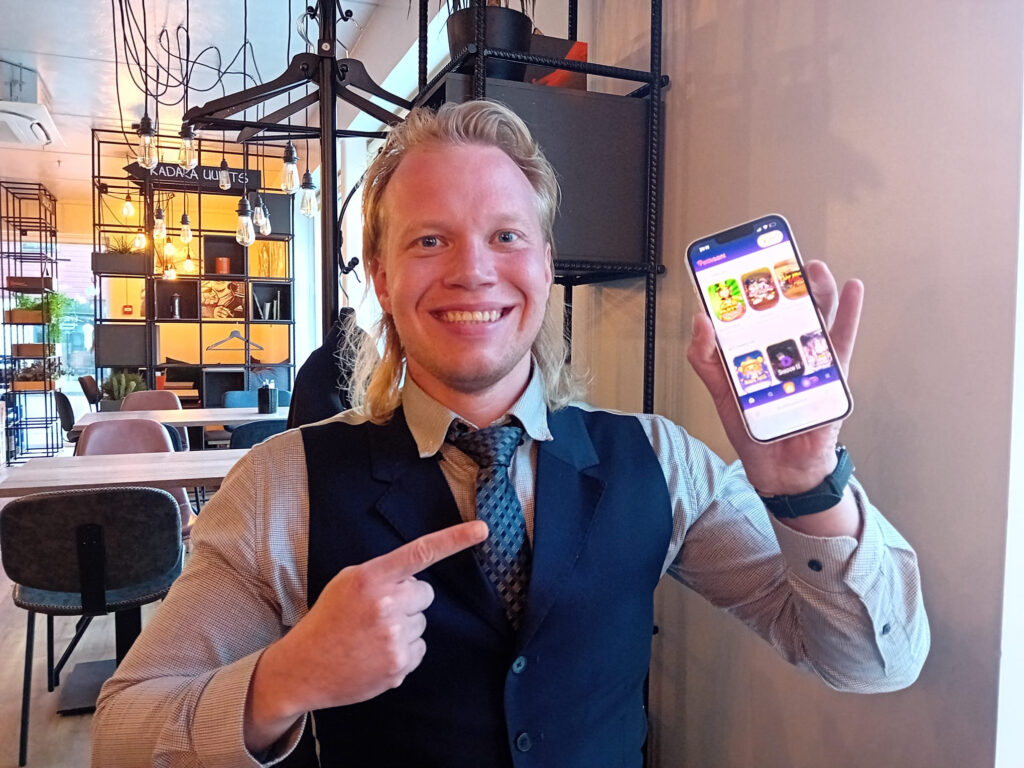 Rahapelisanomat Aleksi Virtanen osoittaa sormella puhelinta. Ruudulla Pelikaani-nettikasino.