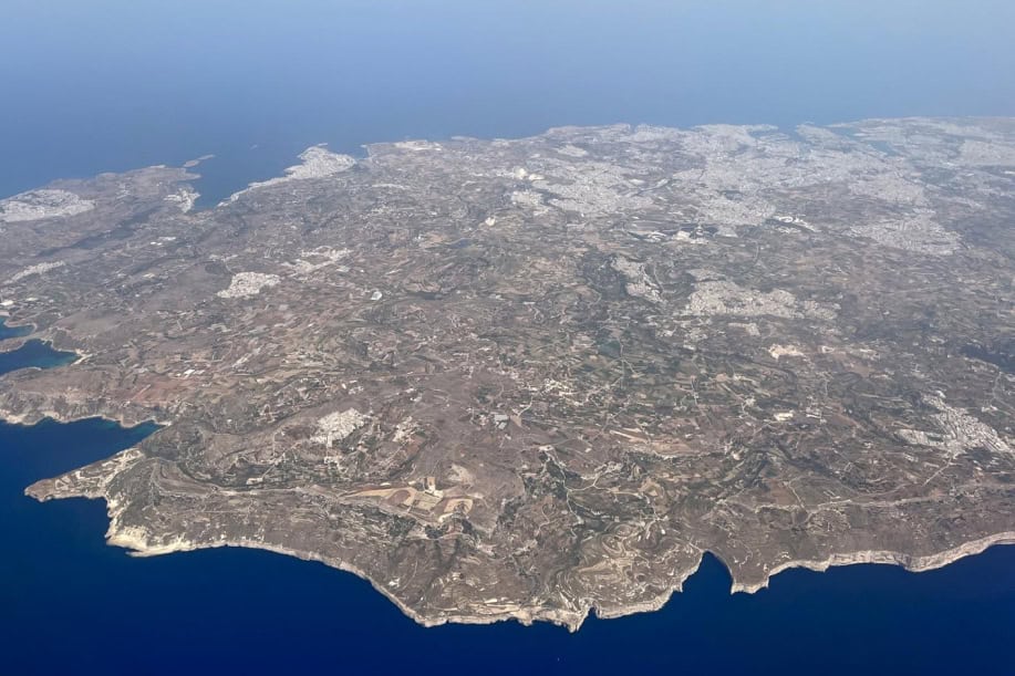 Maltan saari lentokoneesta kuvattuna. Pääkaupunki Valletta ja Grand Harbor näkyvät salmena ja sitä ympyröivänä satamana. Kallioista etelärannikkoa etualalla.