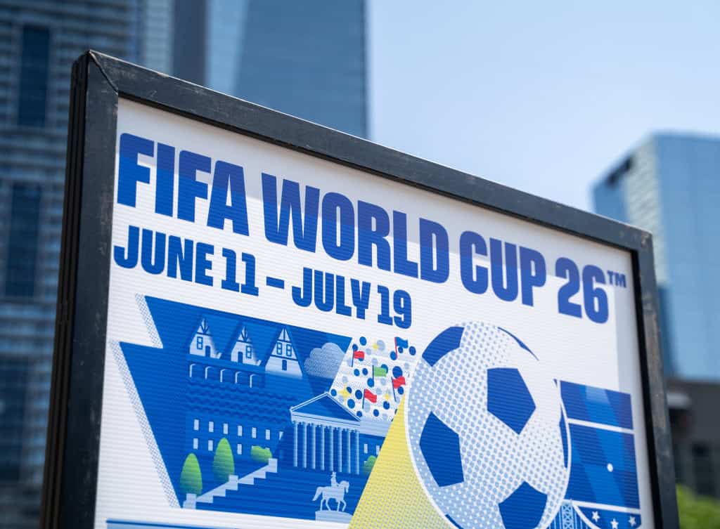 FIFA World Cup 2026 -mainosjuliste, jossa näkyvät päivämäärät June 11 – July 19 sekä jalkapalloteemainen grafiikka modernin kaupungin taustalla