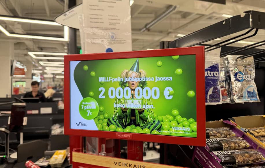 Kaupan kassa AI:lla tehty Milli-mainos kertoo pelin juhlapotin jakavan 2 000 000 euroa koko viikon ajan. Taustalla ruokaostoksia ja kassoja. Tolkkaan kiinnitetty jonkinnäköinen viranomaislupa.