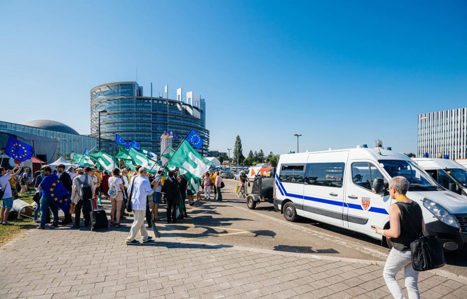 Ihmisiä EU ja Federalistilippujen kanssa Louise Weiss parlamenttirakennuksen edessä. Vieressä poliisiautoja.