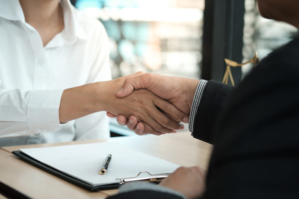 Two hands shaking above a clipboard