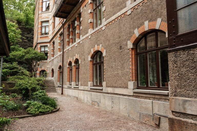 Flerbostadshus med putsad fasad och tegelomfattade fönster på en lummig innergård i Göteborg.
