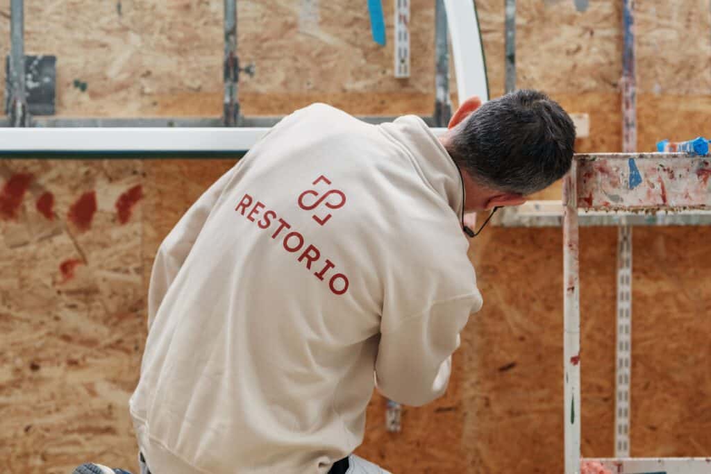Hantverkare från Restorio med ryggen mot kameran målar en fönsterbåge vid målarställning i verkstaden.