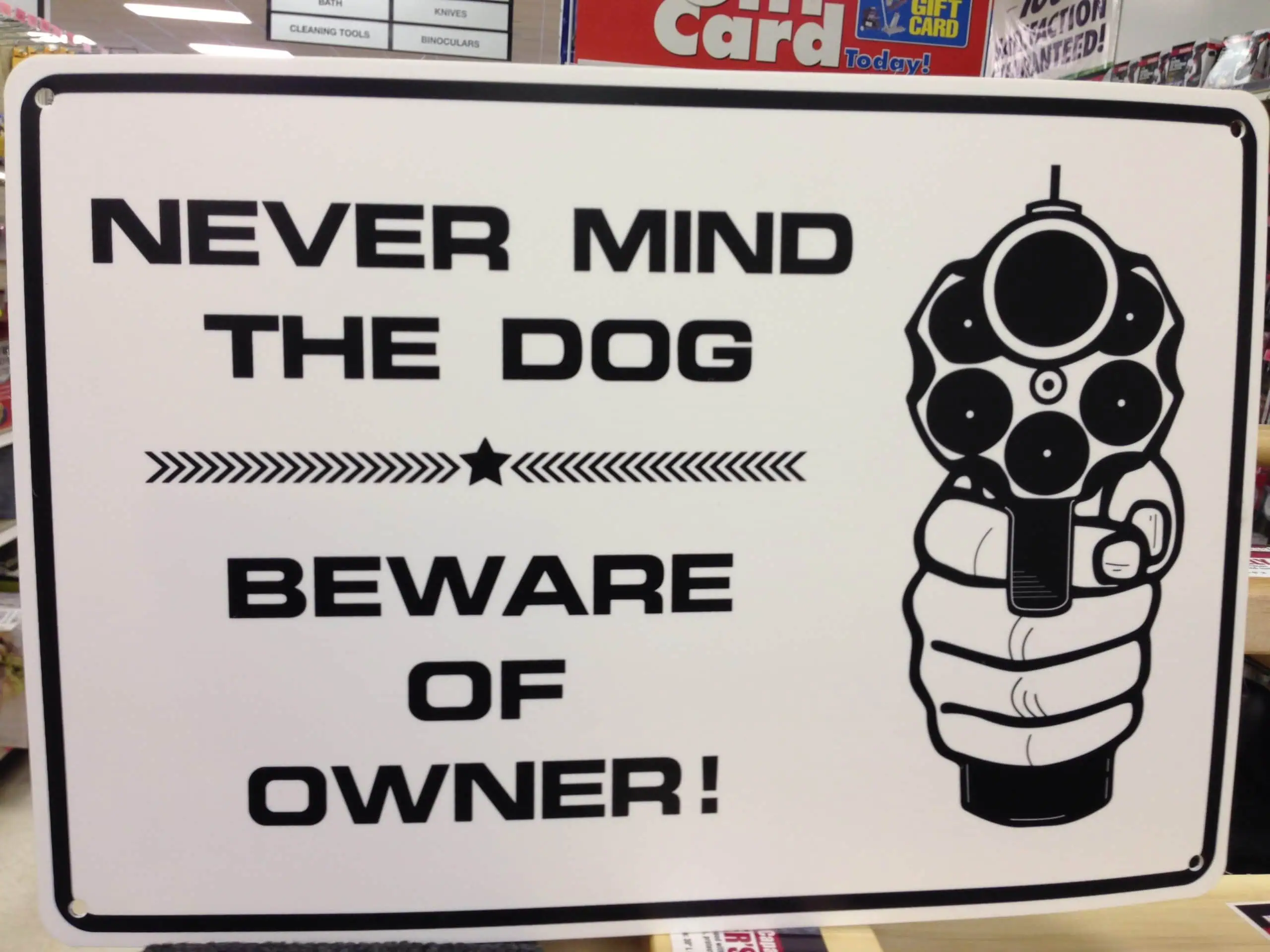 A sign reading NEVER MIND THE DOG BEWARE OF THE OWNER next to a picture of a gun
