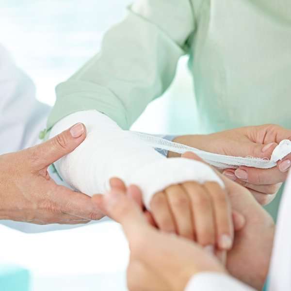 Medical professional bandaging a patient's arm in a clinical setting.