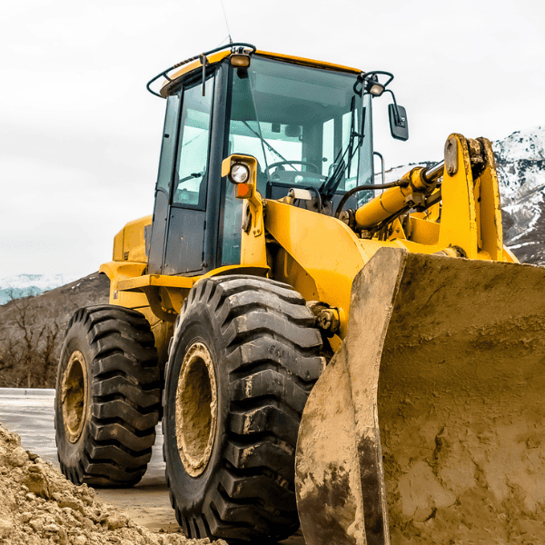 Yellow construction loader on a dirt site with mountains in the background.