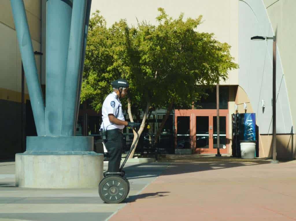 Police officer riding a Segway in an urban area with trees and buildings.