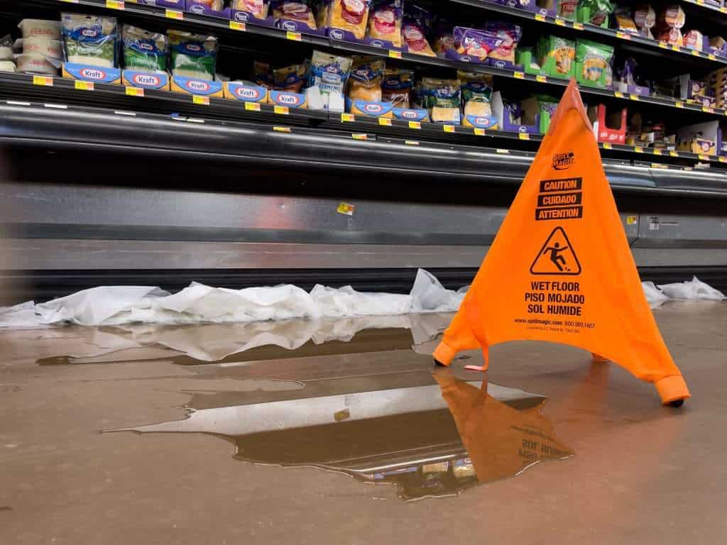 Wet floor with caution sign in grocery store aisle.