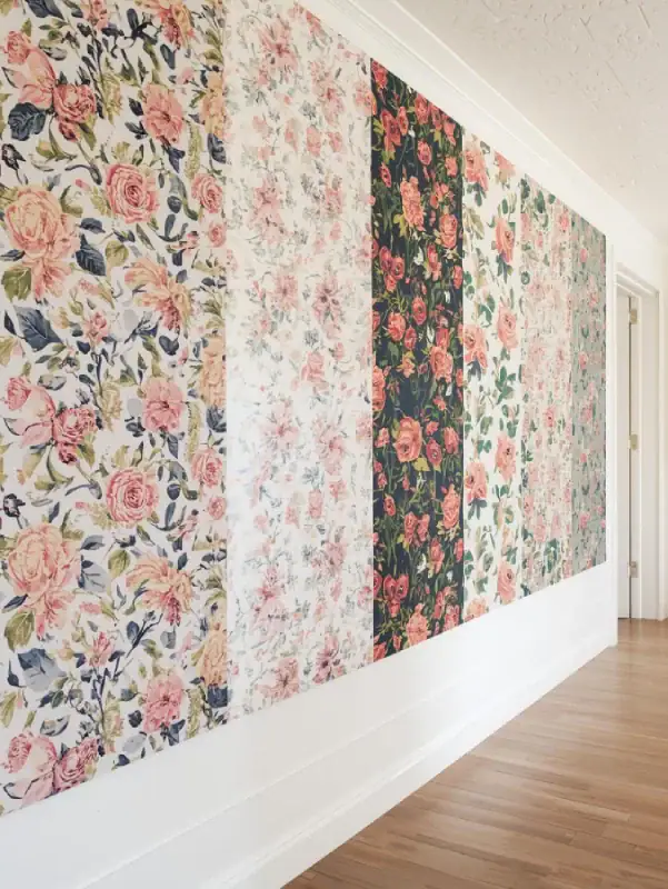 A creative studio or hallway with a gallery of different floral wallpaper panels in various global-inspired styles—vintage English, Moroccan florals, and tropical botanical prints. Eclectic and vibrant.