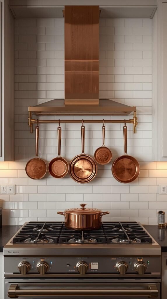 A modern kitchen backsplash scene featuring a polished brass wall-mounted rail with copper cookware hanging neatly above a gas stove.