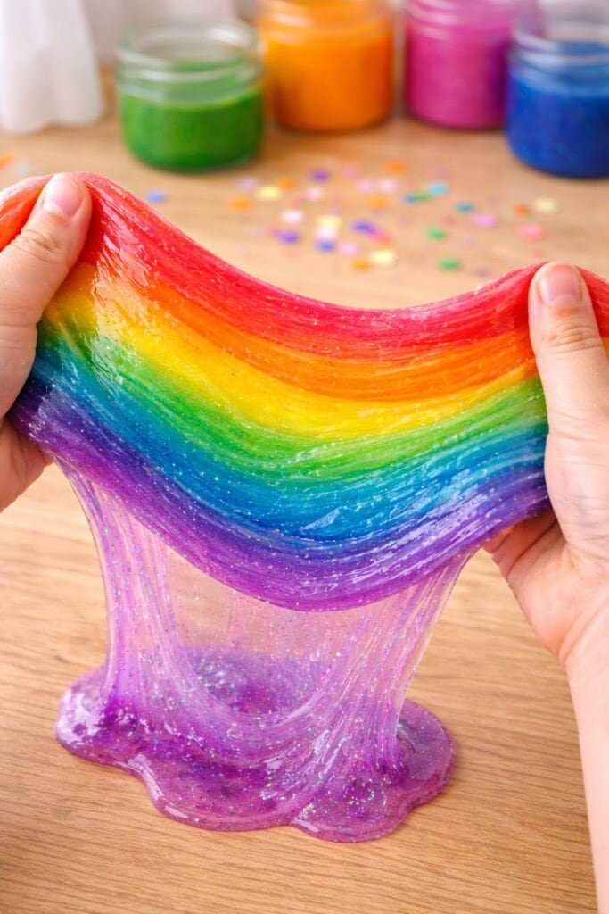 close-up of layered rainbow slime stretched between hands, glossy texture