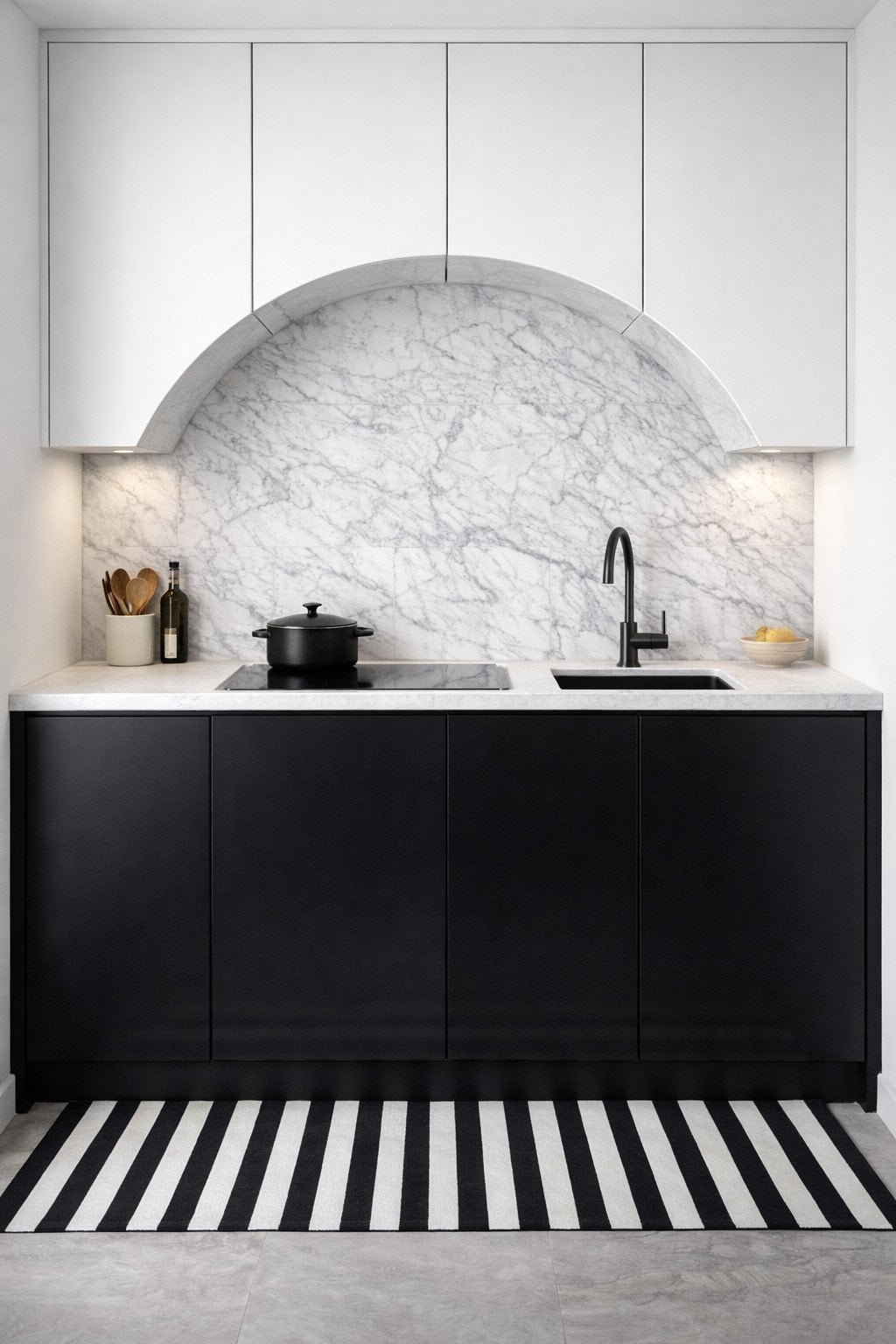 Graphic kitchenette with matte black and white cabinets, arched stone slab backsplash, and striped contrast floor runner.