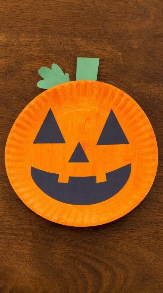 Finished paper plate pumpkin face craft painted orange with construction paper cutout eyes