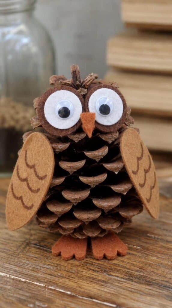 Pinecone owl craft with felt wings and googly eyes on a wood table