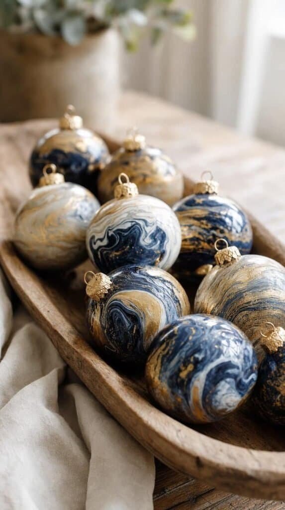 Marbled navy, gold, and white glass bauble ornaments displayed in a wooden dough bowl