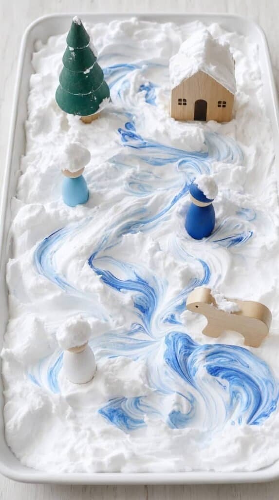 Tray of shaving cream snow with blue paint swirls and small wooden toys