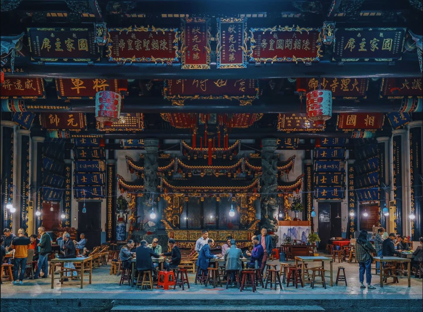 People gathered inside a Chinese ancestral hall with ornate decorations, banners, and altars, preserving Chinese genealogy traditions during a communal event.
