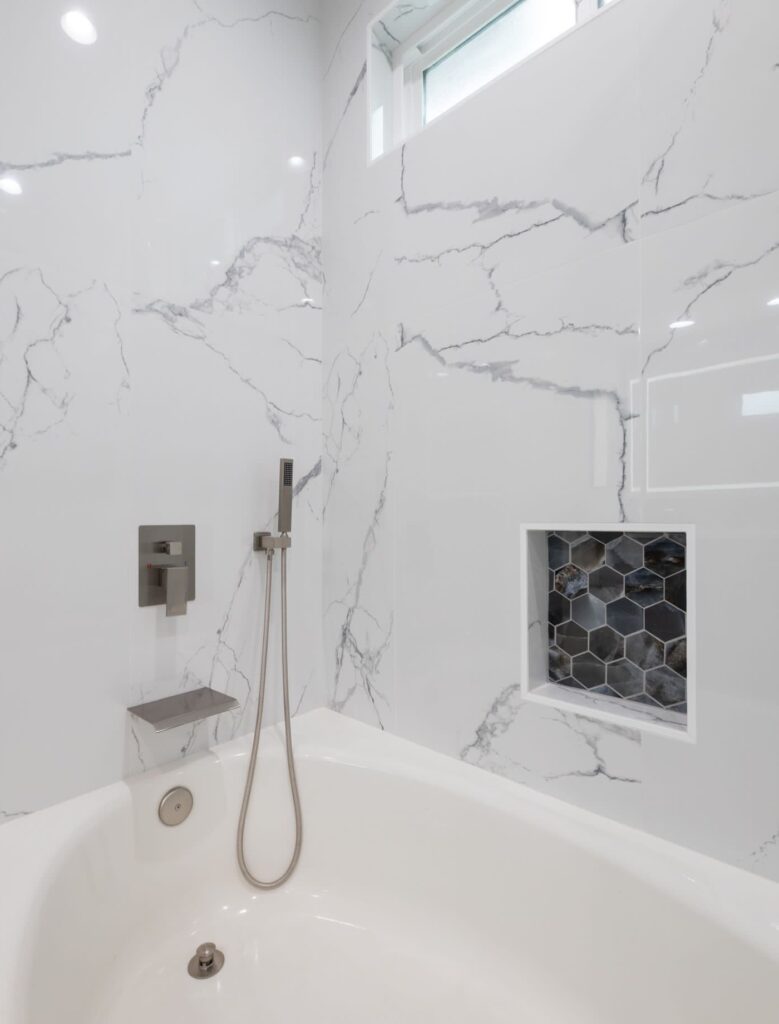 Modern white bathroom with marble-patterned tiles and a bathtub with shower.