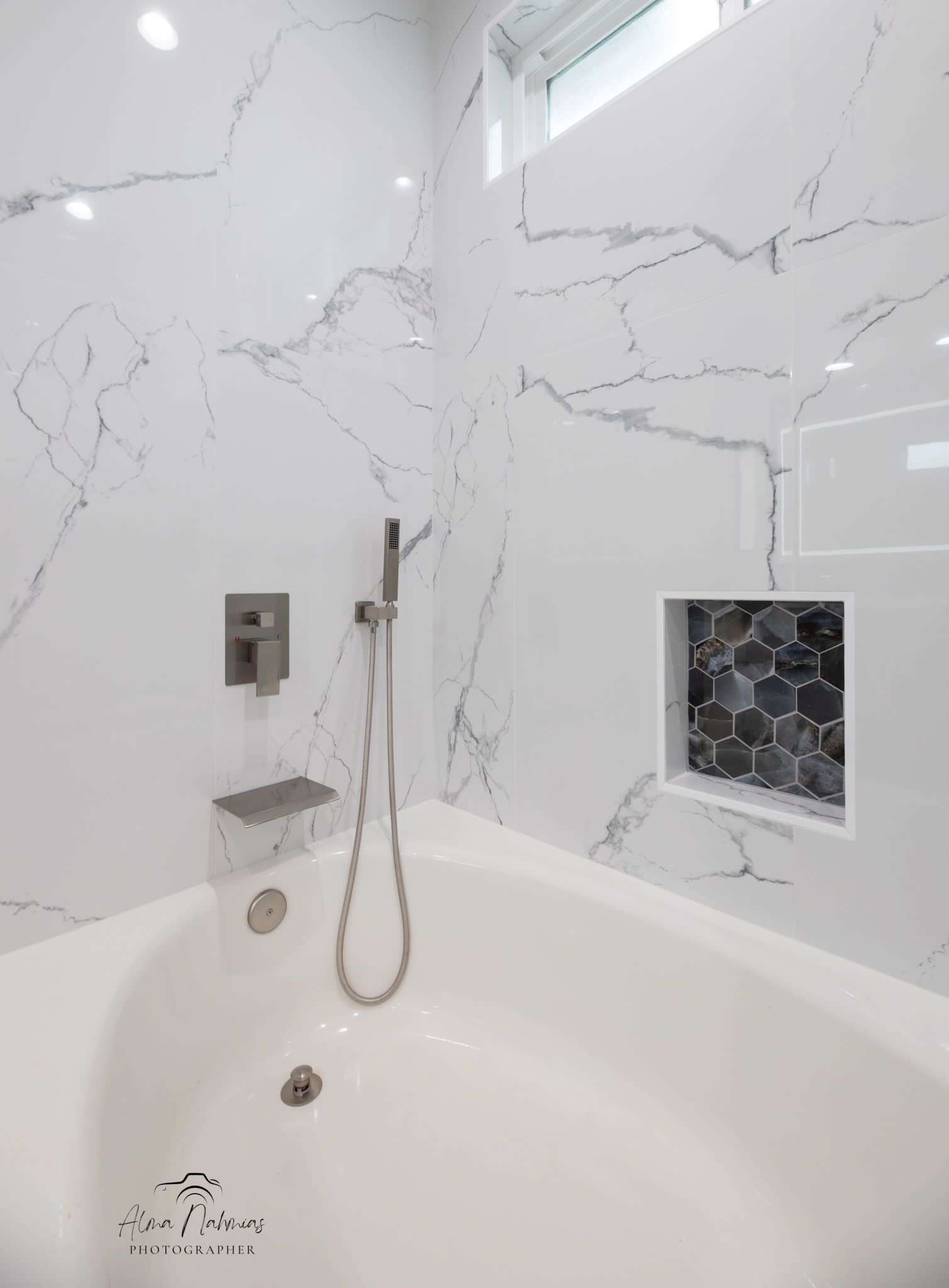 White bathtub with marble-patterned walls and a shower head