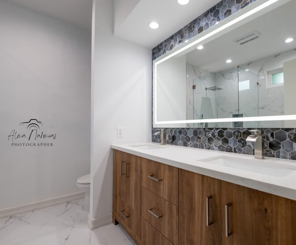 Modern bathroom with double vanity, illuminated mirror, and hexagonal tile accent wall.