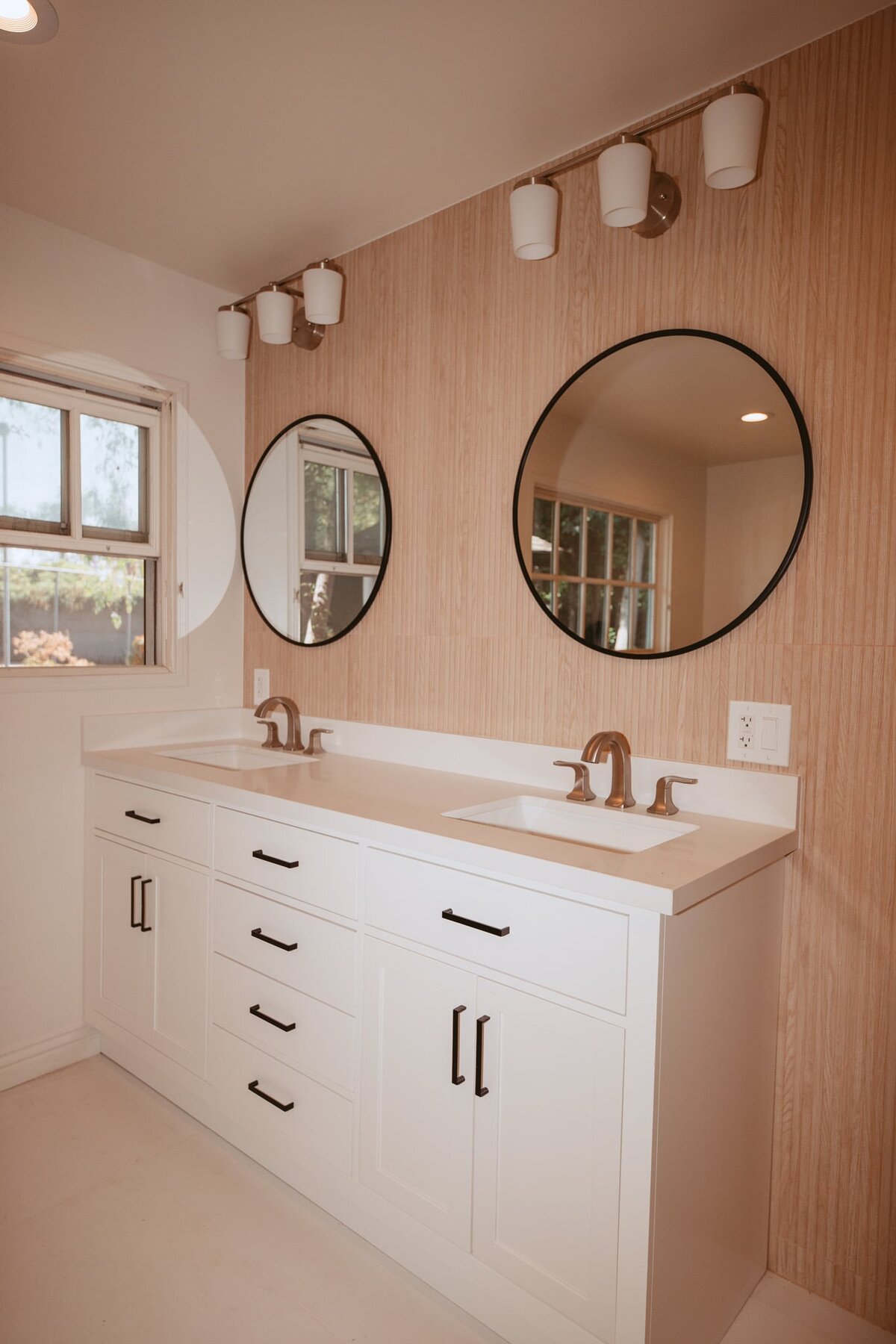 Modern bathroom with double vanity, round mirrors, and wood-paneled wall.