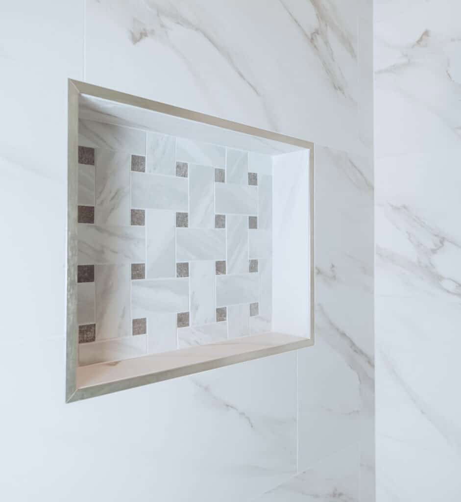 Built-in shower niche with decorative tile against marble-patterned wall tiles.