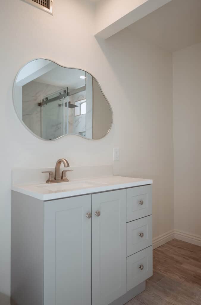 Modern bathroom vanity with a unique mirror and light gray cabinets.