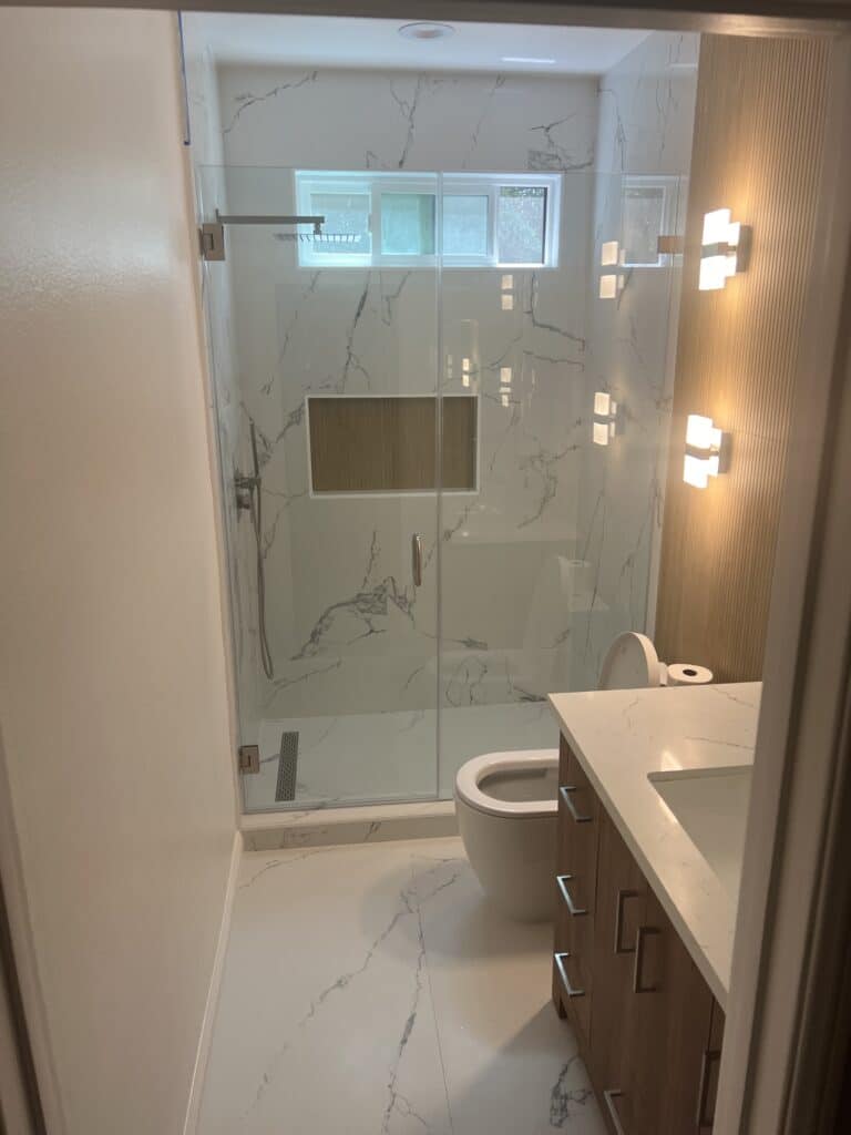 Modern bathroom with glass shower, white marble, and wooden vanity