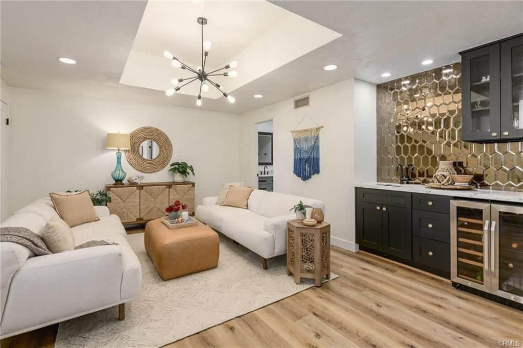 Modern living room with white sofas, a bar, and a unique chandelier.