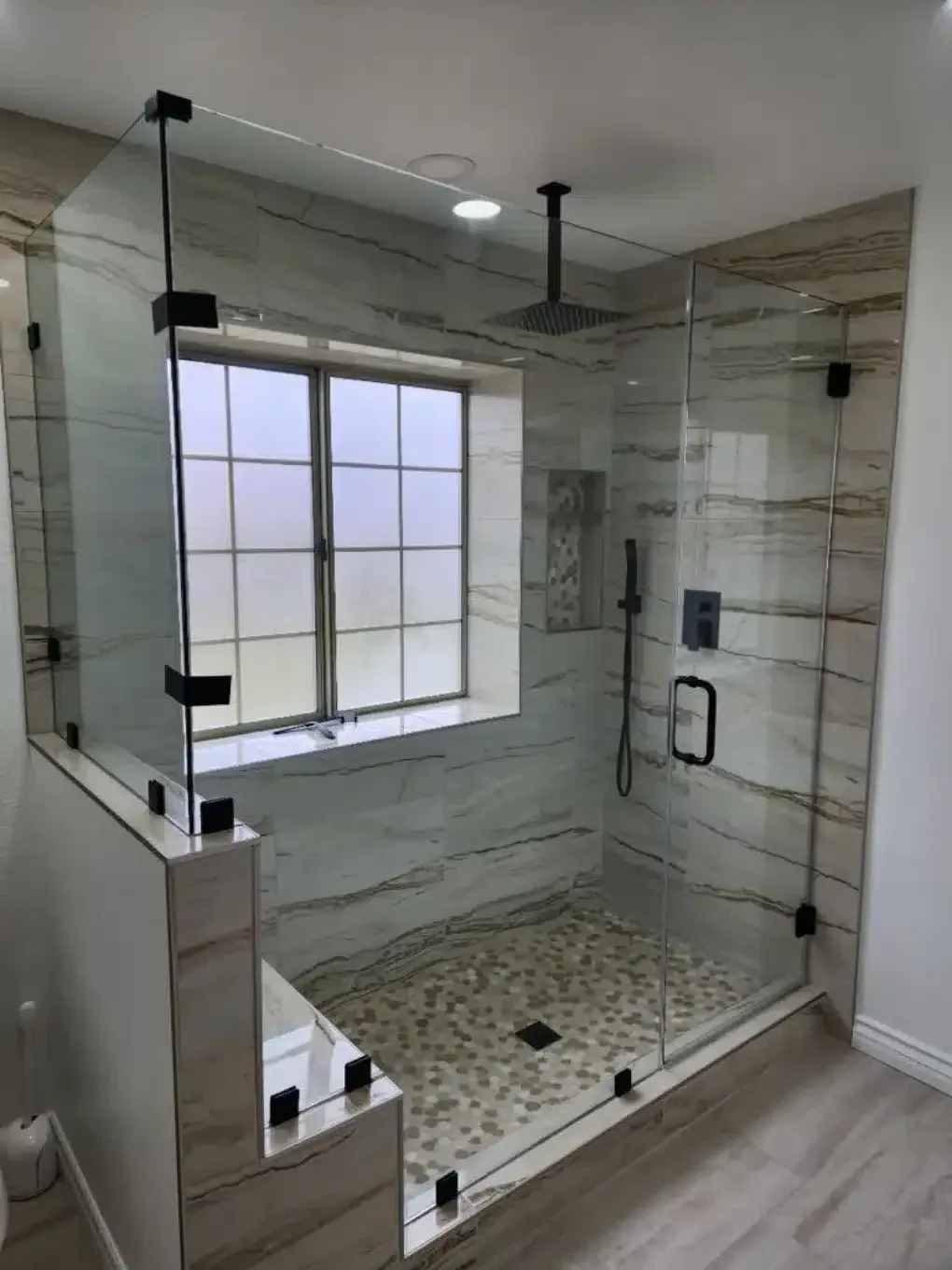 Modern walk-in shower with glass walls, tiled interior, and pebble floor.