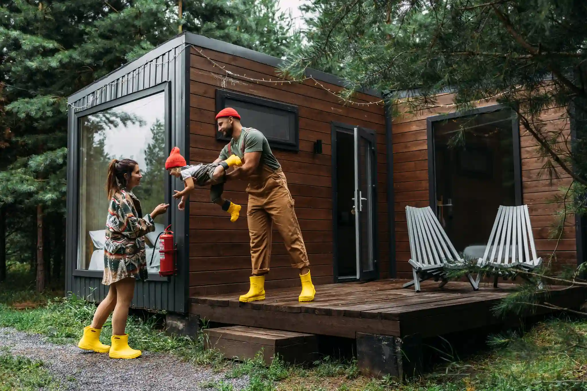 Man holding a child, woman looking at them, in front of a modern cabin