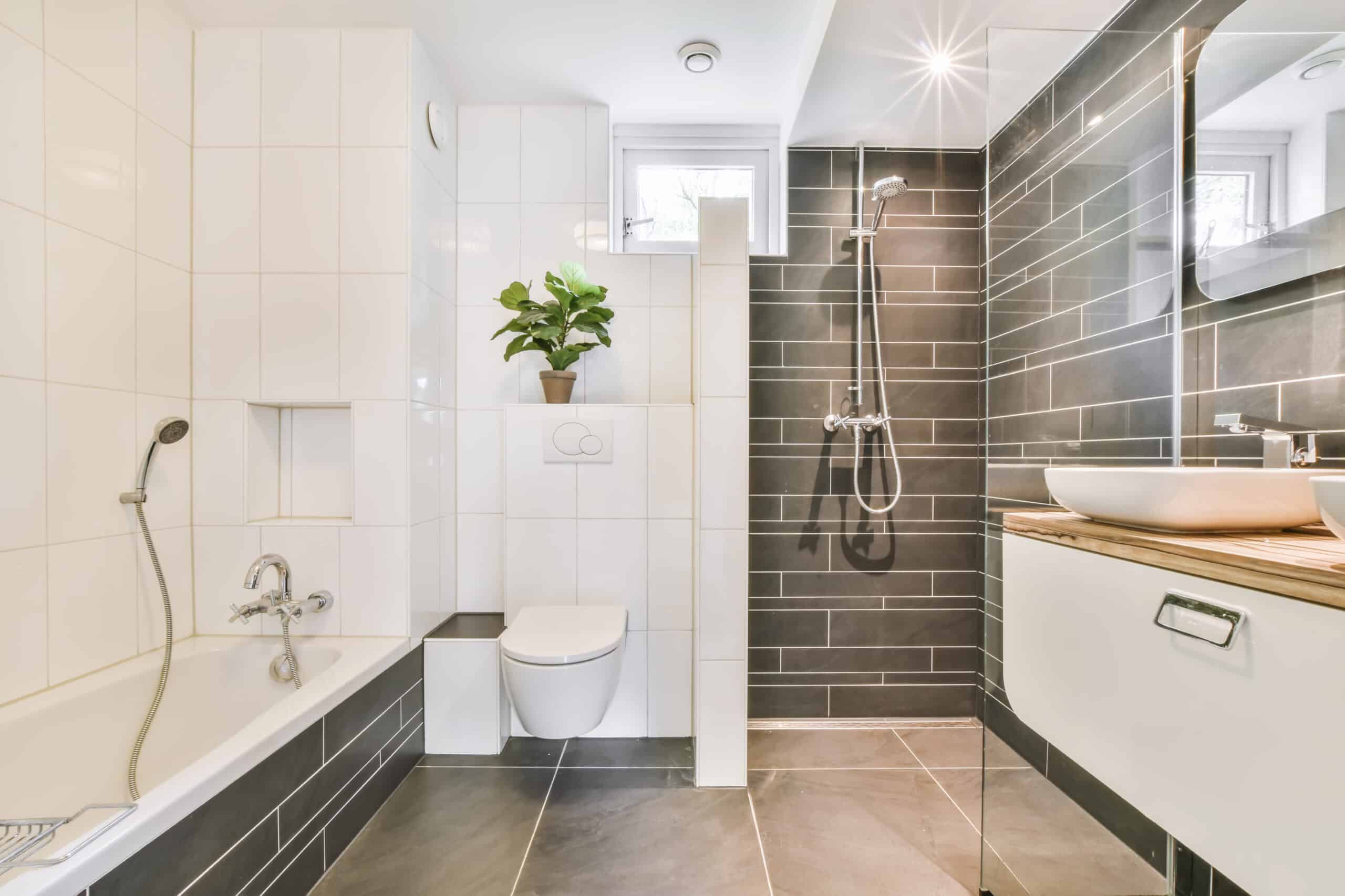Modern bathroom with white bathtub, toilet, and dark tiled shower area.