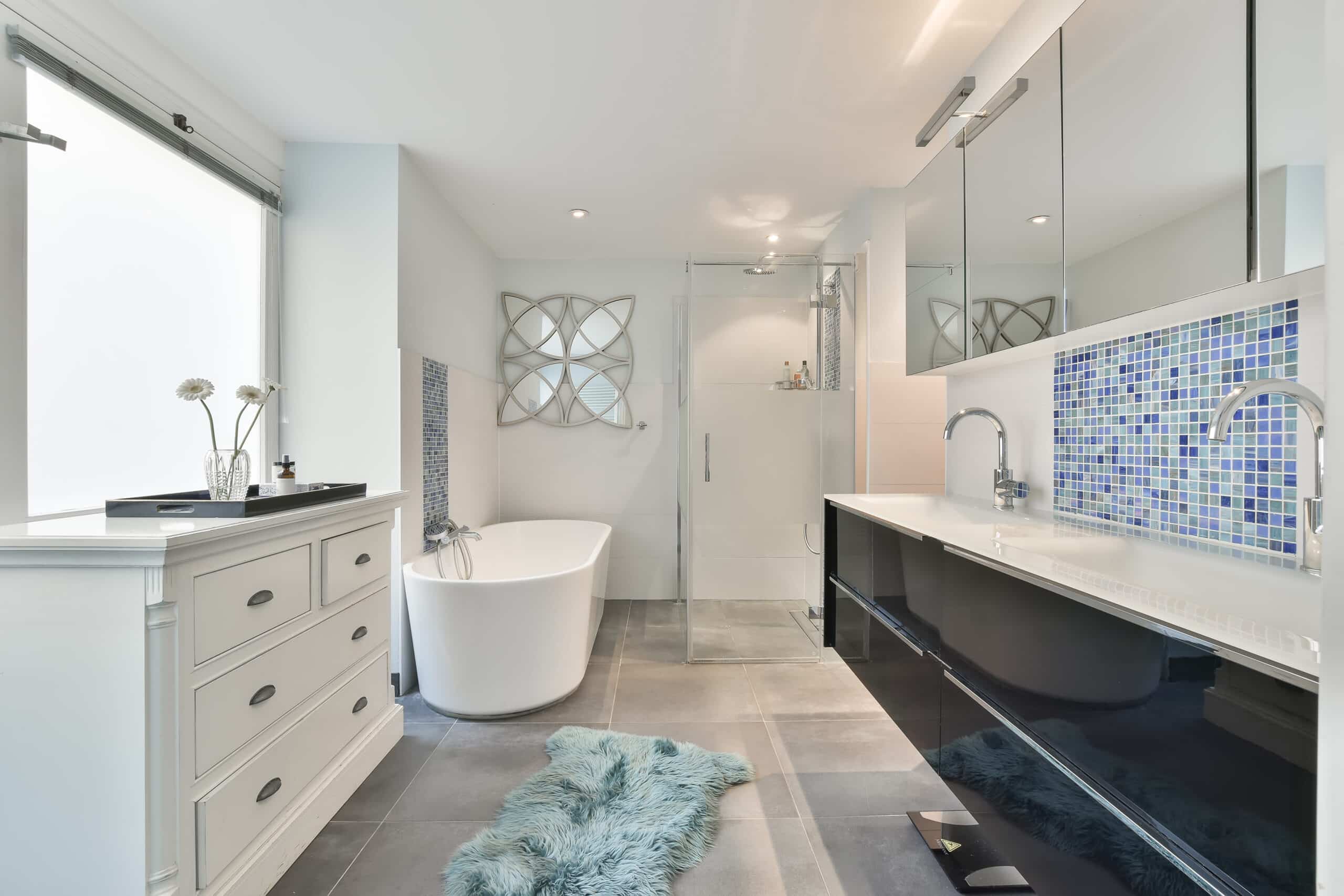 Modern bathroom with white tub, glass shower, and vanity with blue tiles.