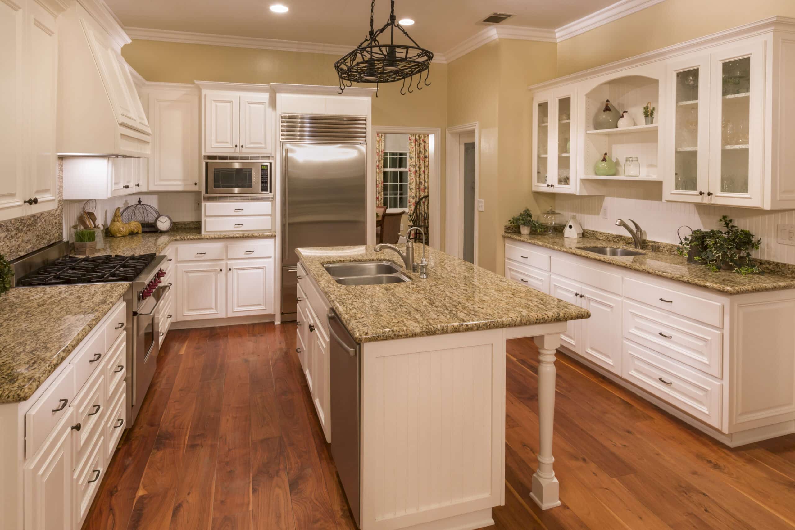 Well-lit kitchen with white cabinets, granite countertops, and hardwood floors.