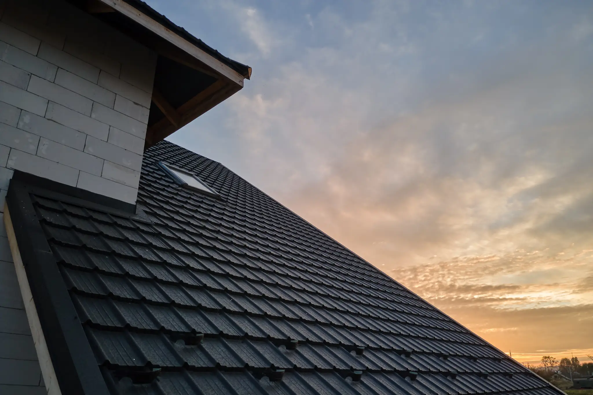 New dark gray metal tile roof on a house under a cloudy sky