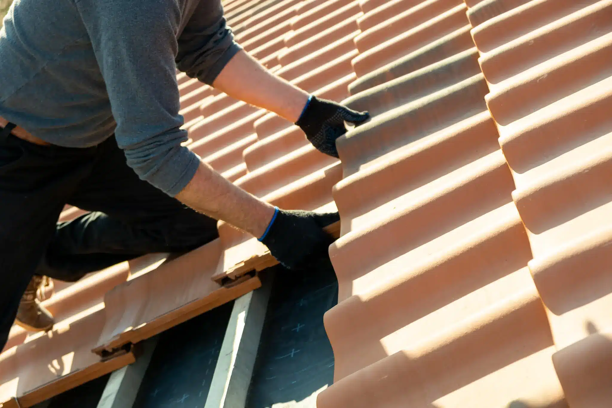 Person installing terracotta roof tiles on a sunny day