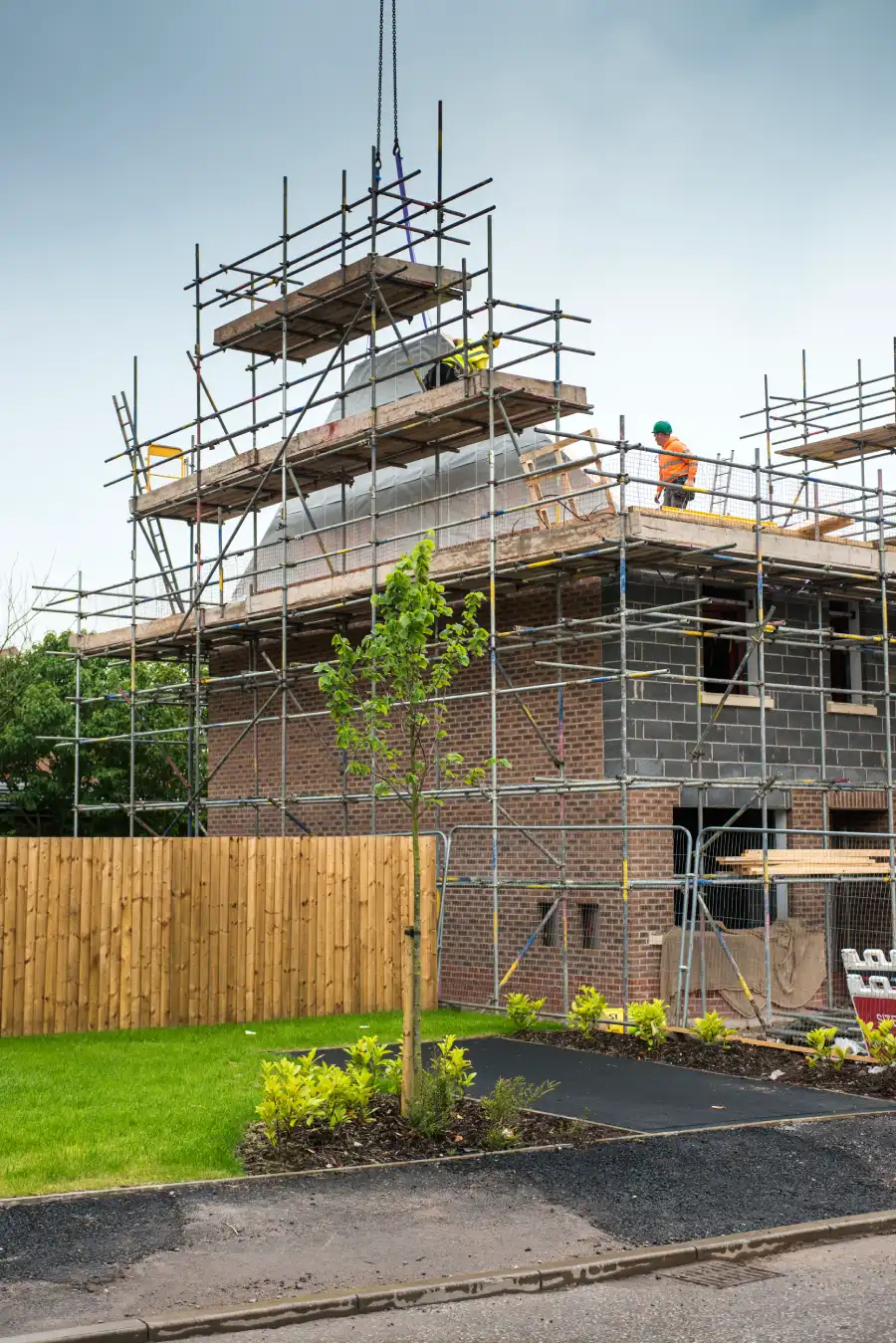 Construction site with scaffolding around a brick house under a cloudy sky