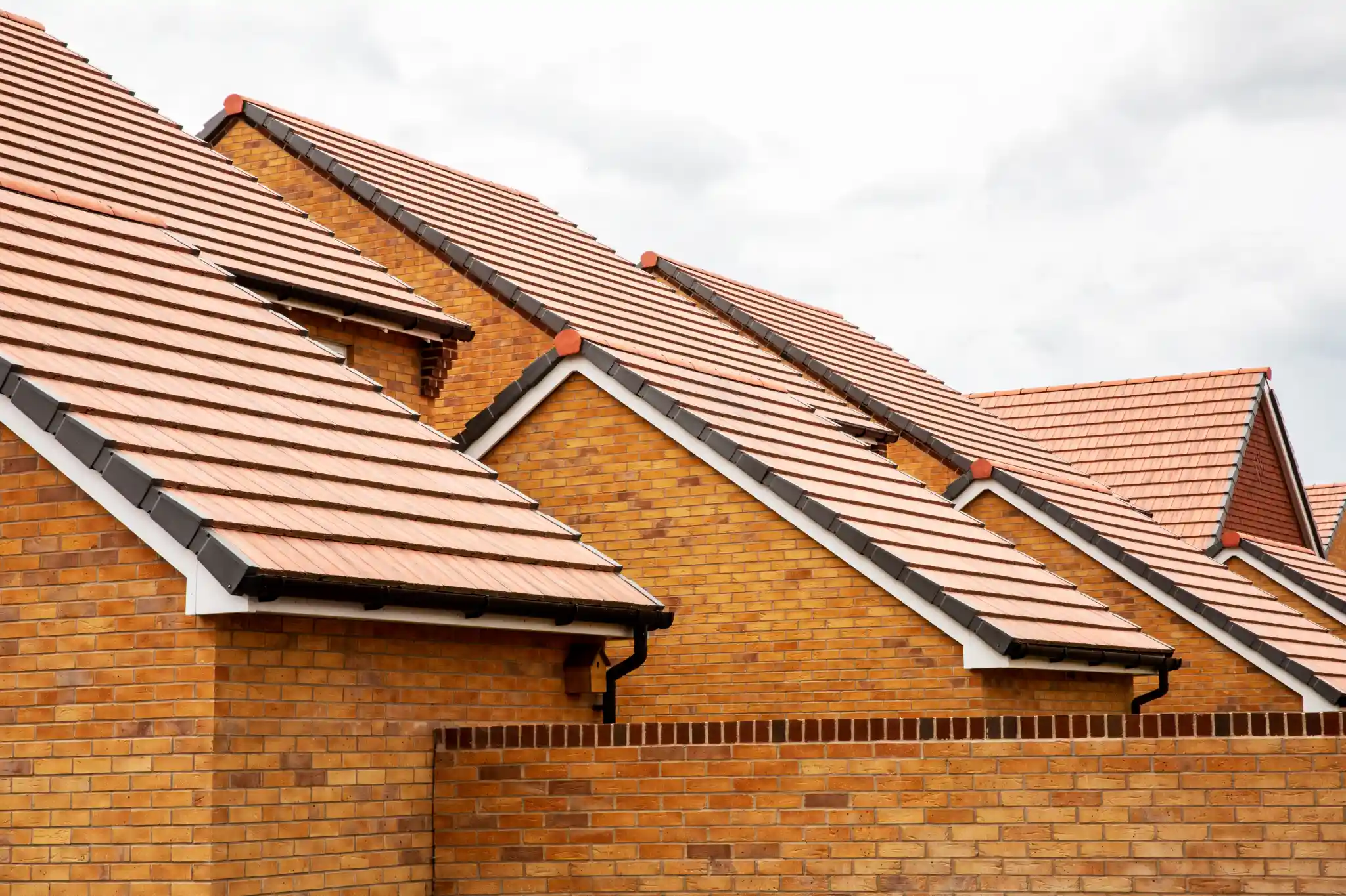 Close-up of new brick houses with red tiled roofs under a cloudy sky.