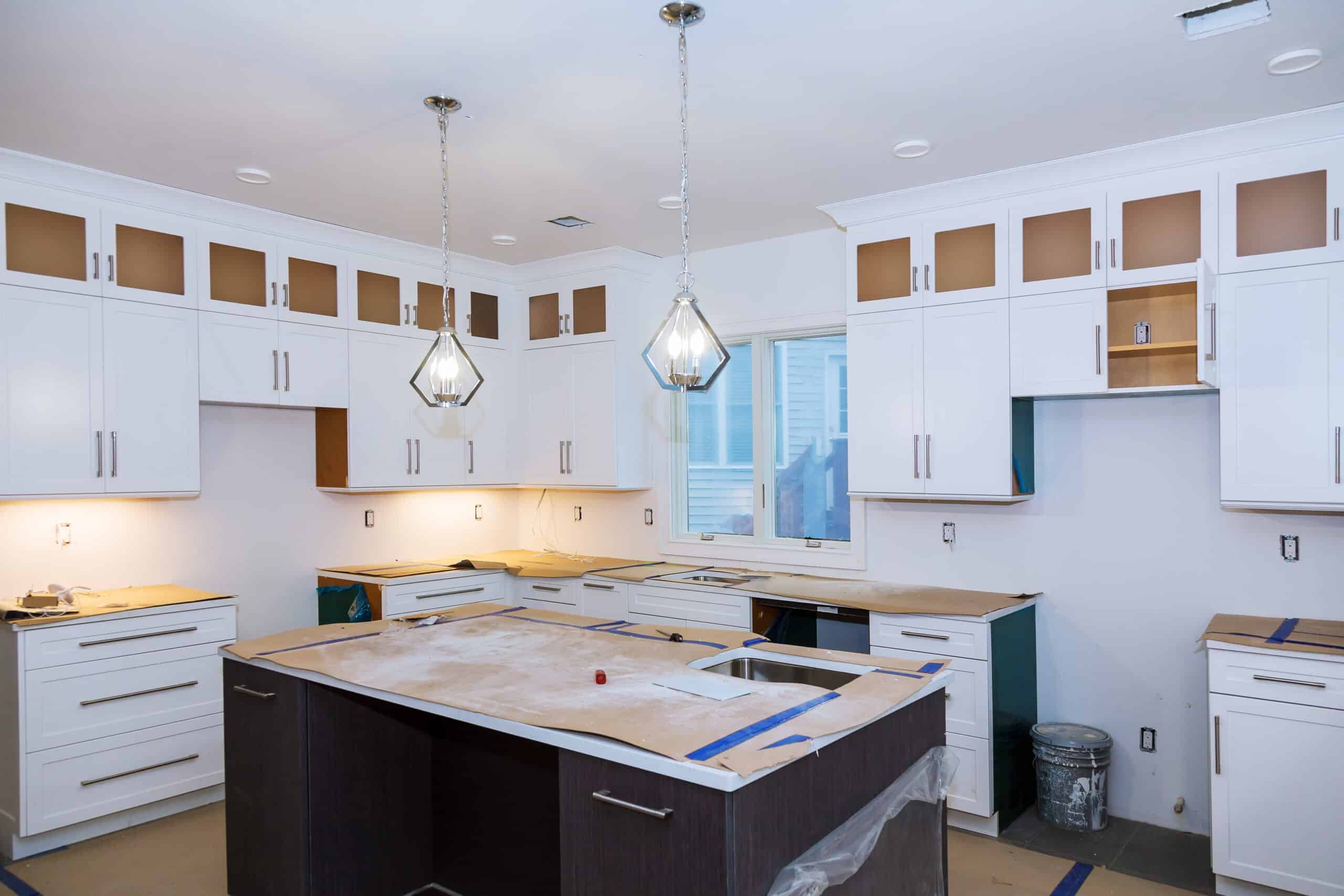 Kitchen under construction with white cabinets, dark island, and pendant lights