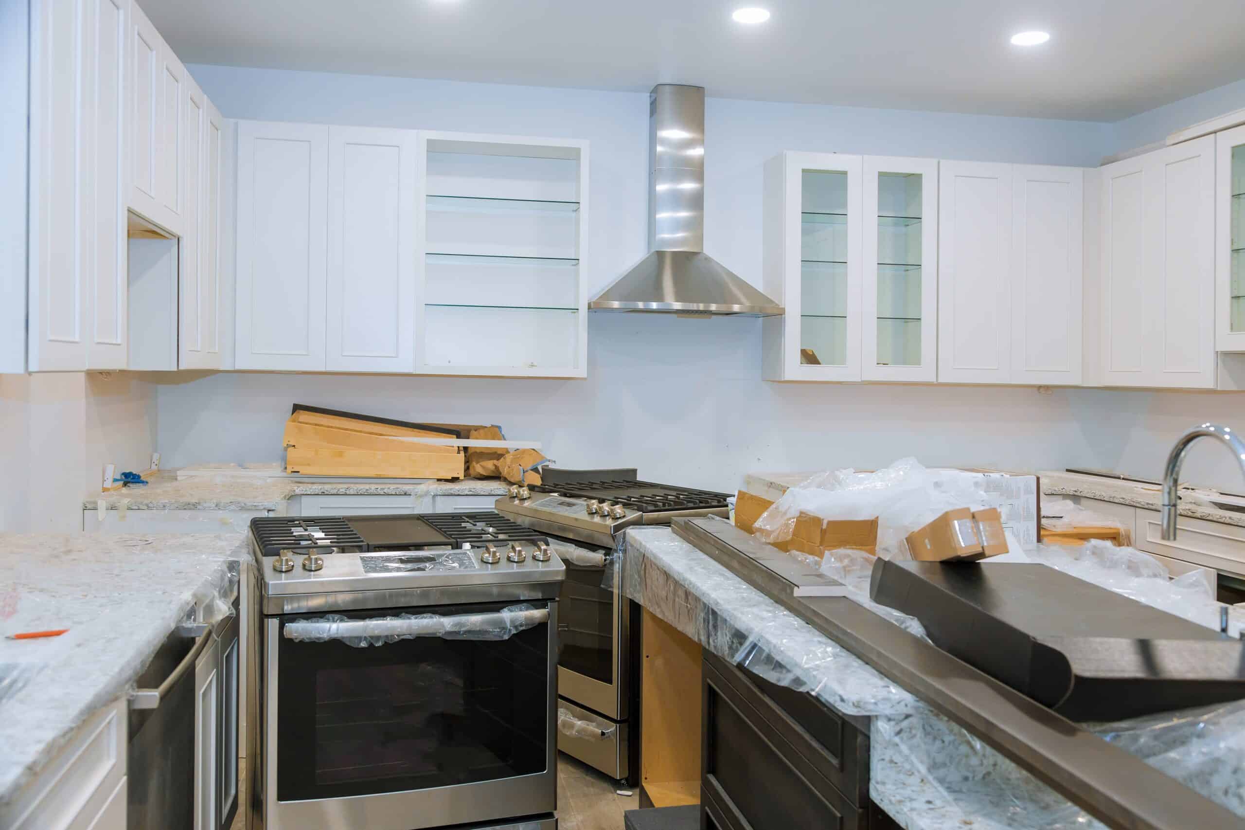 Kitchen under construction with white cabinets, stainless steel appliances, and countertops.