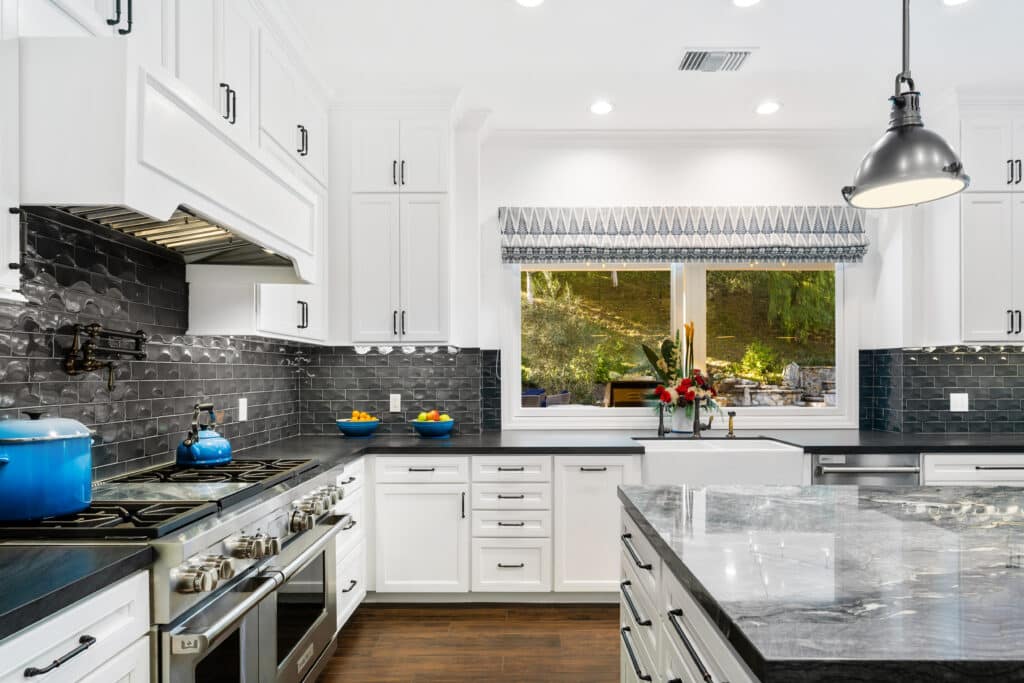 Modern white kitchen with dark countertops, stainless steel appliances, and a window.