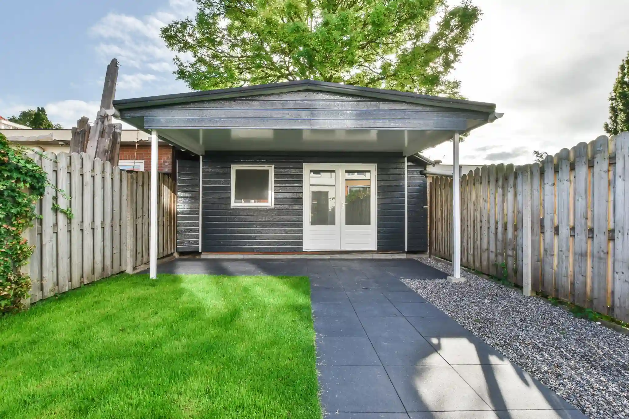 Small dark gray shed with white trim and a covered patio.