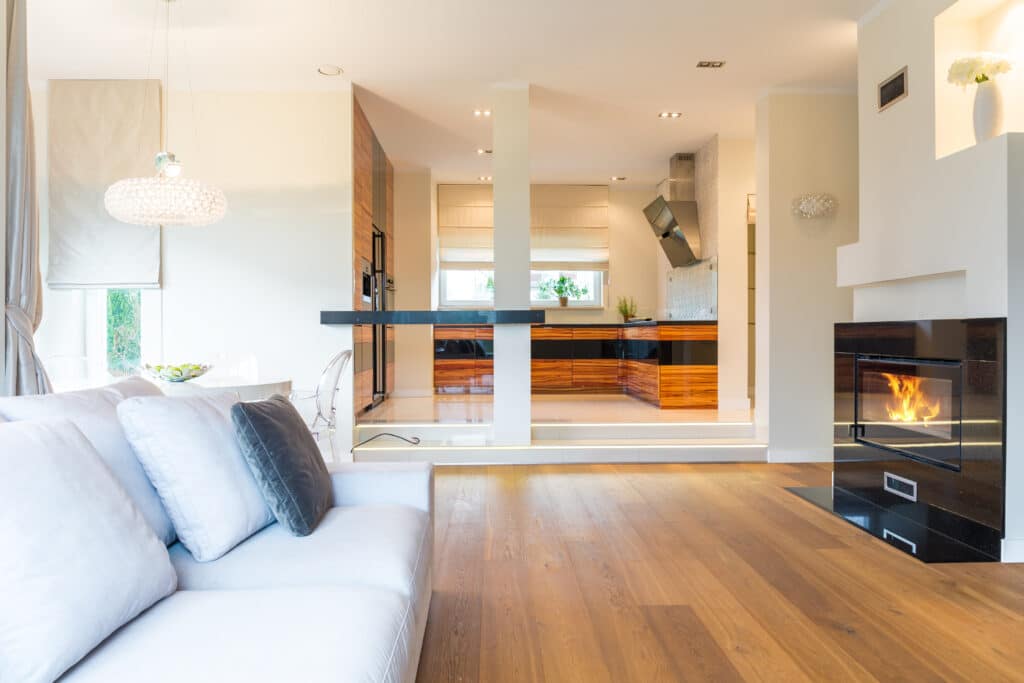 Modern open-plan living room with white sofa, fireplace, and kitchen visible.