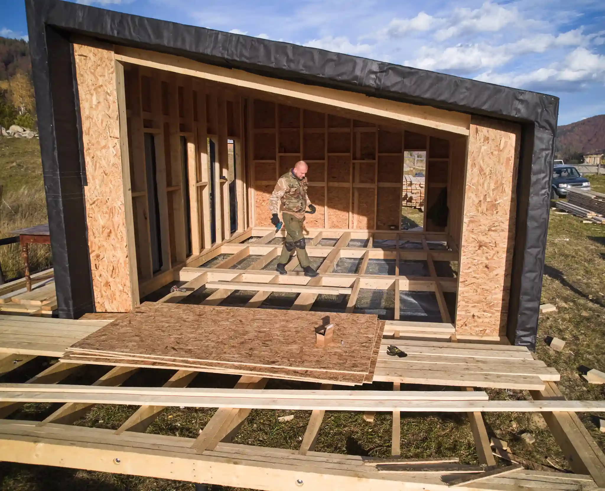 Man walking inside a wooden house frame under construction on a sunny day