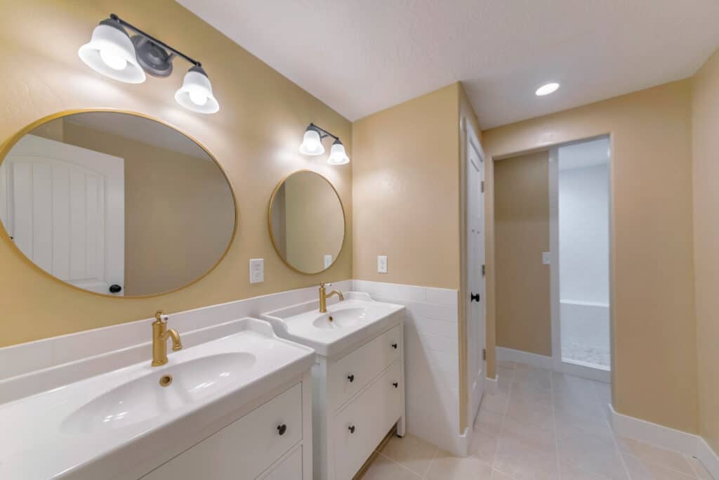 Two white sinks with gold faucets in a bathroom with two mirrors.