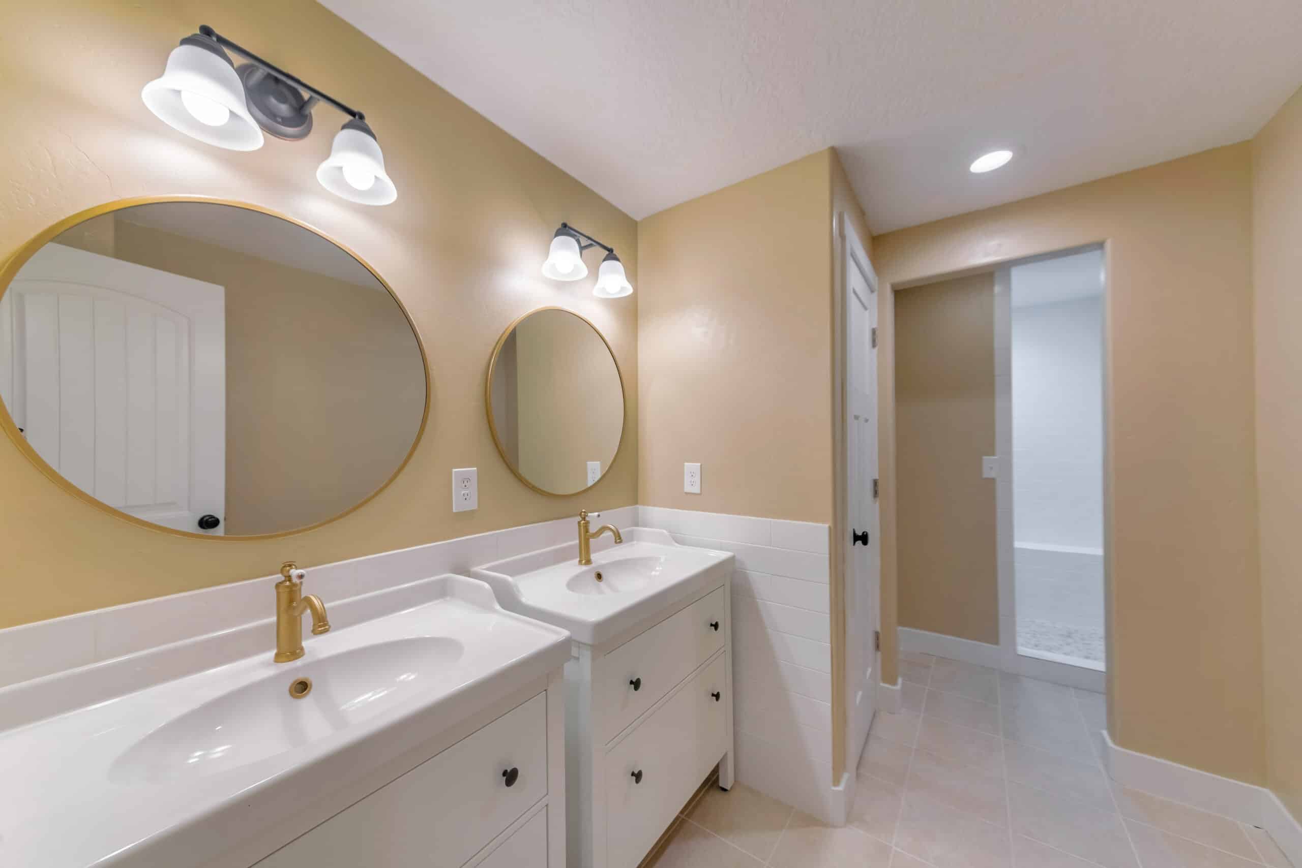 Two white sinks with gold faucets in a bathroom with two mirrors.