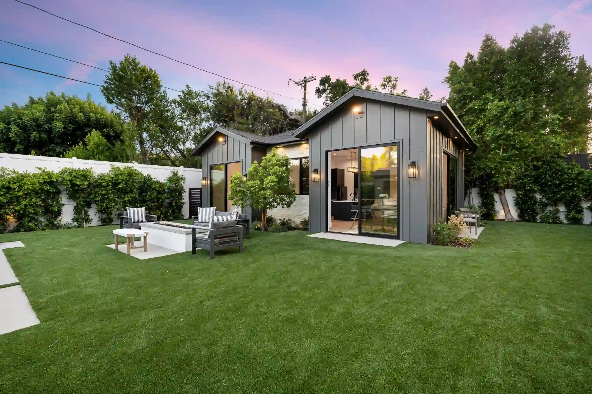 Modern house with a green lawn and outdoor seating under a twilight sky.