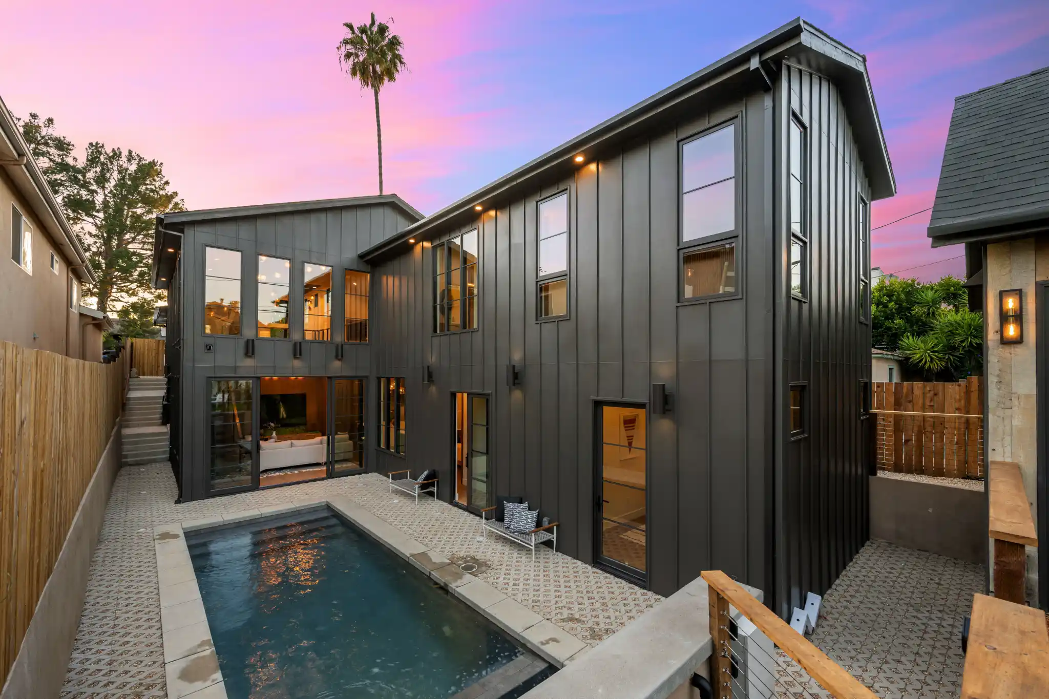 Modern dark gray house with a swimming pool under a colorful sunset sky