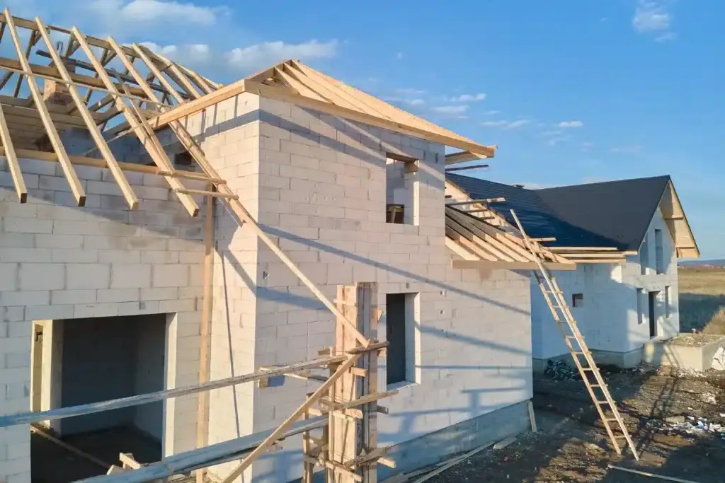 Two houses under construction with visible wooden roof frames and white brick walls